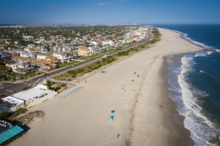 A strip of sandy beach between blue waves and town with road and houses